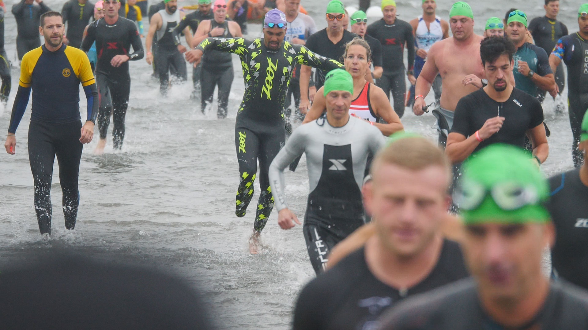 triathletes run through water in a crowd